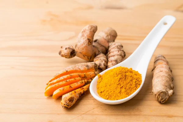 Fresh and grounded turmeric roots on wooden surface — Stock Photo, Image