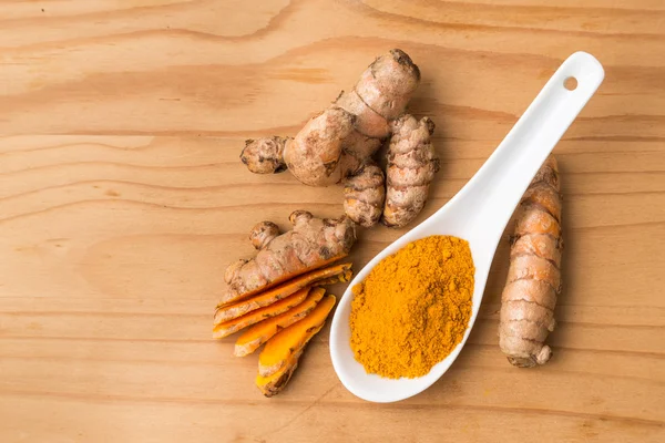 Fresh and grounded turmeric roots on wooden surface — Stockfoto