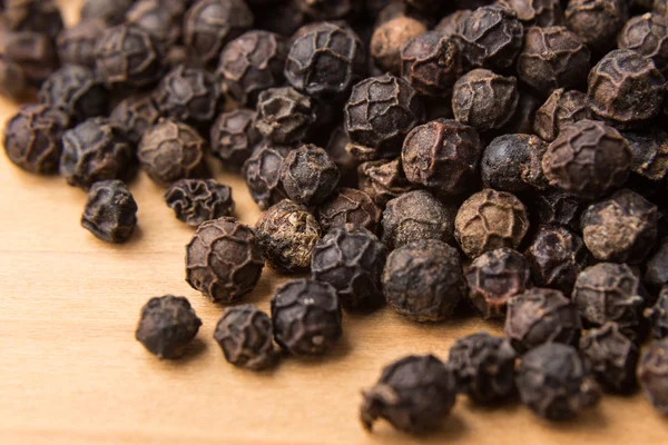 Heaps of black pepper corns on wooden surface Stock Photo