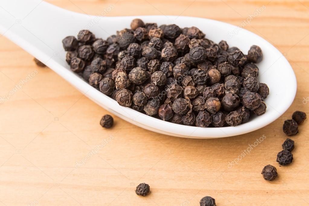 Spoonful of black pepper corns on wooden surface