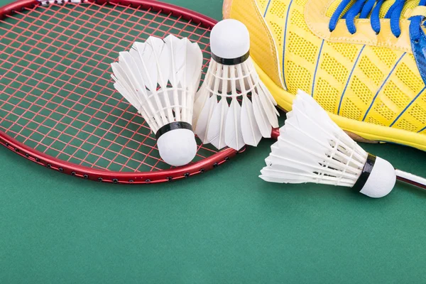 Três badminton shuttlecock com raquete e sapatos na quadra verde — Fotografia de Stock