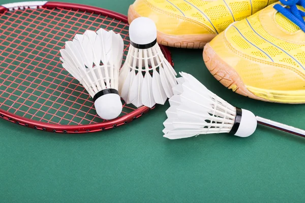 Três badminton shuttlecock com raquete e sapatos na quadra verde — Fotografia de Stock