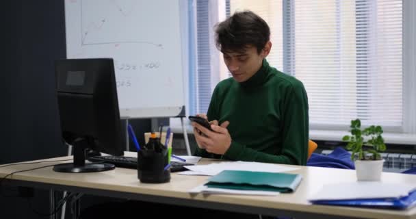 Lächelnd glücklich junge kaukasische Mann verwenden Telefon im Büro — Stockvideo