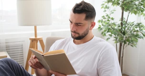 一个英俊的男人在家里看书 — 图库视频影像