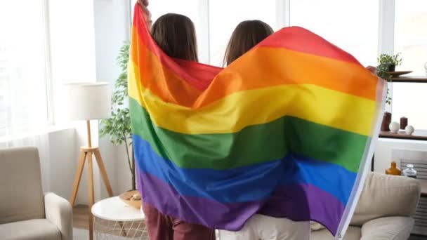 Pareja LGBT envuelta en la bandera del arco iris bailando en casa — Vídeo de stock