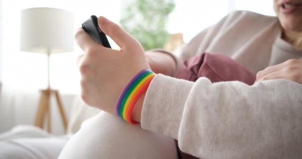 Detailní záběr duhové stuhy na ruce, mluvící LGBT pár na pohovce — Stock video