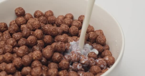 Il latte viene versato in una ciotola completamente bianca con palline di cereali al cioccolato — Video Stock