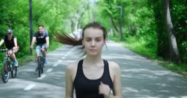 Genç bir kadının spor giyim kuşamında yolda koşarkenki görüntüsü.