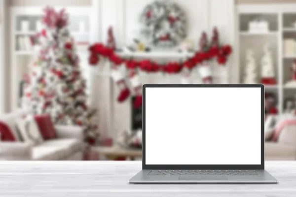 白い木製のテーブルの上に空白の画面のラップトップコンピュータ クリスマスの装飾が施されたモダンな居心地の良い家庭のリビングルーム ホームオフィスのデスクワークスペース コピースペースをモックアップします 冬の販売 オンラインショッピング ストックフォト