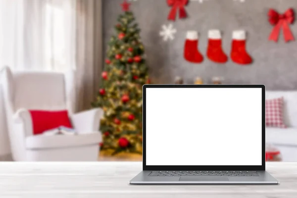 白い木製のテーブルの上に空白の画面のラップトップコンピュータ クリスマスの装飾が施されたモダンな居心地の良い家庭のリビングルーム ホームオフィスのデスクワークスペース コピースペースをモックアップします 冬の販売 オンラインショッピング ロイヤリティフリーのストック画像
