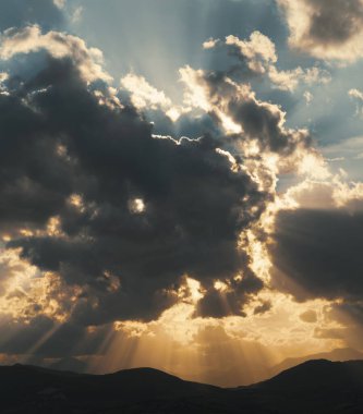 Gün batımında gökyüzü ve bulutlarda güneş ışığı, ufukta dağlar