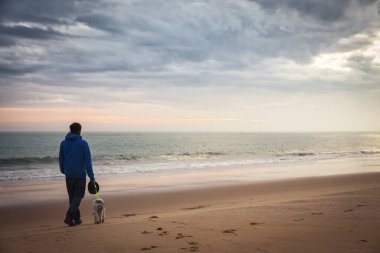Yavrusuz köpeğini sahilde gezdiren adam.