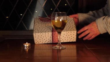 Bir bardak beyaz şarapla hediyeyi açan eller.