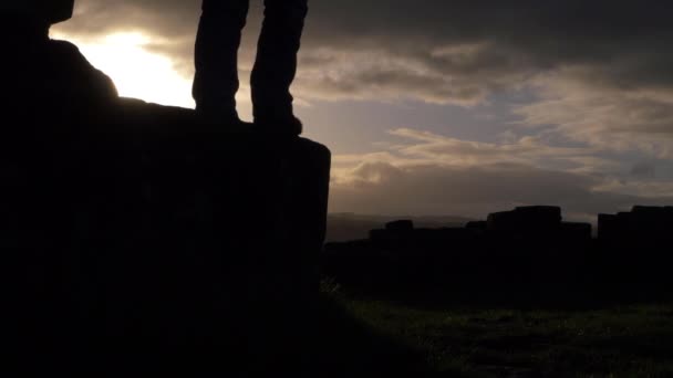 Kobieta skacze ze skał przed zachodem słońca i chmurami — Wideo stockowe