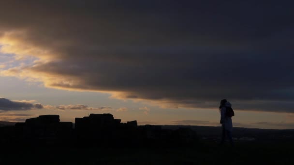 Kayalık arazide gün batımı ve bulutlu arka planda yürüyen bir kadın. — Stok video