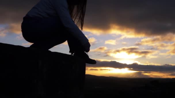 Wanita terletak di lanskap berbatu terhadap matahari terbenam dan awan — Stok Video
