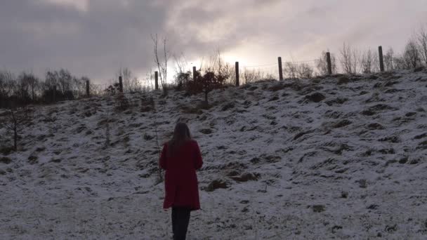 Kvinna går i snö i skymningen bär röd rock — Stockvideo
