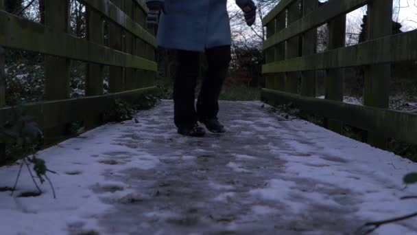 Frau läuft über klapprige alte Holzbrücke, die mit Schnee bedeckt ist — Stockvideo
