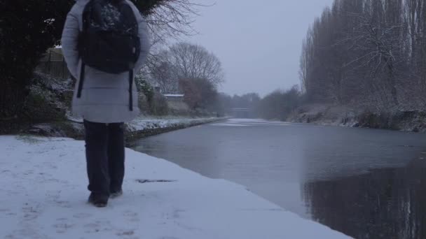 Randonneuse solitaire sur le sentier du canal alors que la neige tombe — Video