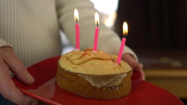 Elleri yanan mumlarla doğum günü pastası tutuyor.