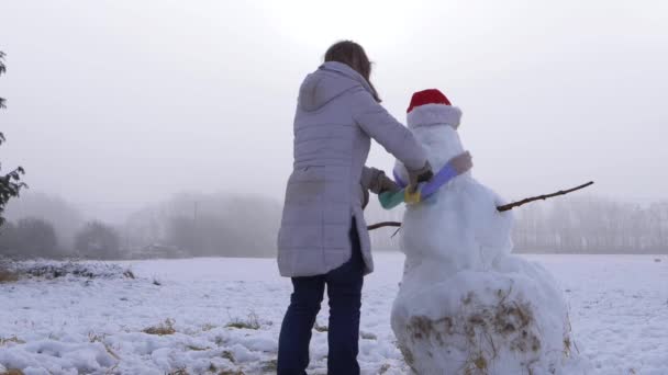 Lycklig kvinna sätter halsduk på en snögubbe — Stockvideo