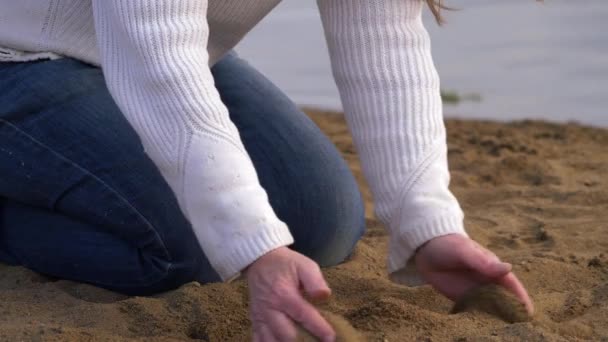 Woman scoops up sand at waters edge — Stock Video