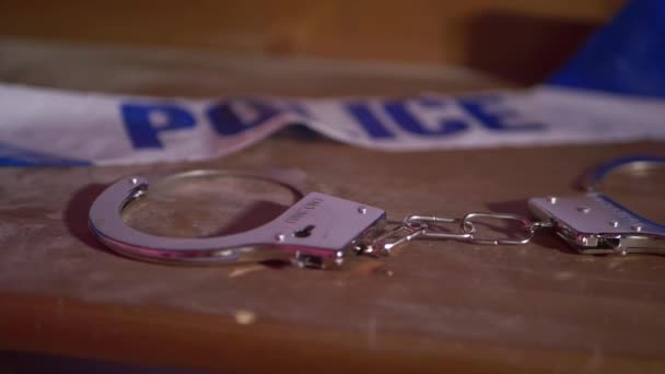 Χειροπέδες και αστυνομική ταινία σε ξύλινο τραπέζι — Αρχείο Βίντεο