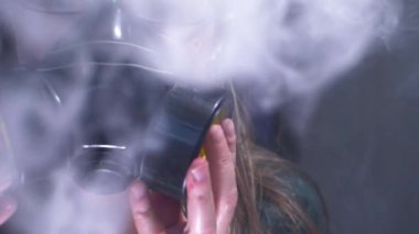Duman dolu oda, arka planda gaz maskesi takan kadını ortaya çıkarıyor.