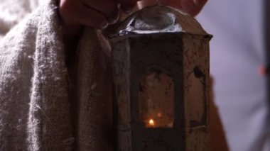 Elleri mum aleviyle kirli eski bir feneri tutuyor. 