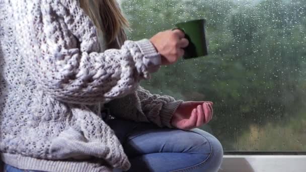 Vrouw kijkt regen uit een raam met mok thee — Stockvideo