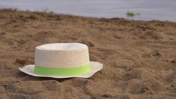 Floppy straw hat left by water side in the sand — Stock Video