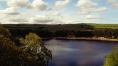 Ağaçlar ve tarım arazileri, Peak District Ulusal Parkı 'ndaki gölü çevreleyen mavi gökyüzü geniş zoom insansız hava aracı seçici odak noktası.
