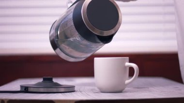 Çaydanlıktan kupaya sıcak su dökülüyor. Orta boy, yavaş çekim seçici odak noktası.