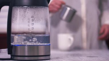 Bir su ısıtıcısında su kaynatan bir kadın arka planda sıcak bir içecek yapıyor. Yavaş çekim seçici odaklanma.