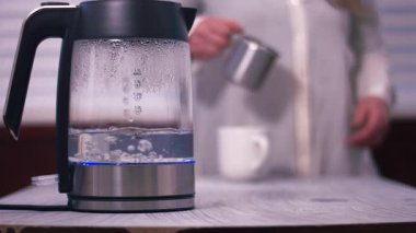 Sıcak suyla kaynayan çaydanlık. Arka planda süt döken kadın. Yavaş çekim seçici odak noktası.