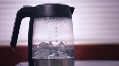 Sıcak su, cam çaydanlıkta kaynıyor. Orta boy, yavaş çekim, seçici odak noktası.