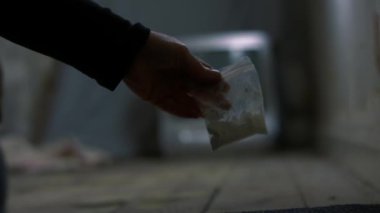 Terk edilmiş evde uyuşturucu torbası tutan bir uyuşturucu satıcısı. Yakın çekim odağı seçici.