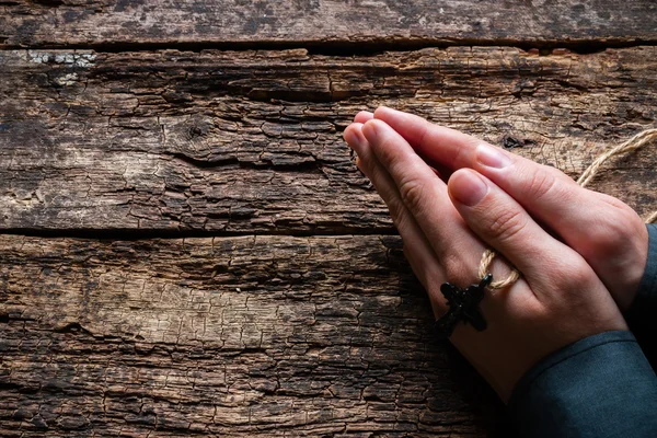 Uomo che prega con una croce tra le mani su uno sfondo di legno — Foto Stock