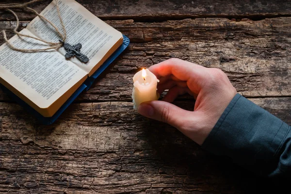 Man holding a candle in front of the bible and cross selective focus — Stock Photo, Image