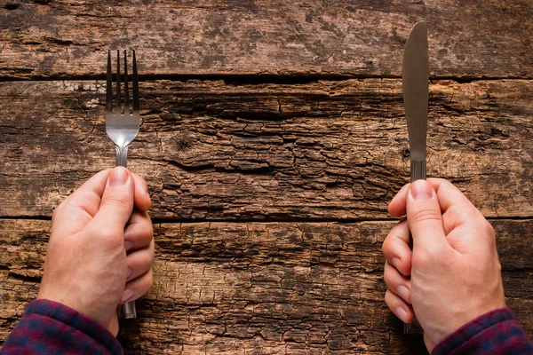 Man holding a knife and fork on a wooden background — Stock Photo, Image