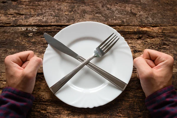 Man refuses to eat spoon and fork on a plate stacked in the shape of a cross — Stock Photo, Image