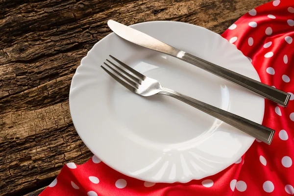 Empty white plate and cutlery on red napkin — Stock Photo, Image