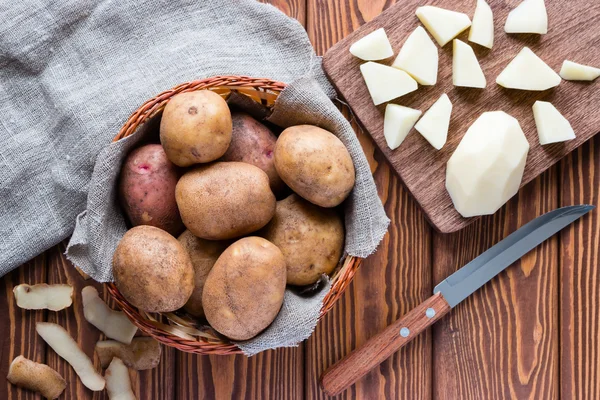 Rohe Kartoffeln im Korb und geschälte Kartoffeln auf einem Schneidebrett — Stockfoto