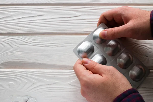 Uomo apre un pacchetto di compresse di antibiotici su uno sfondo bianco — Foto Stock