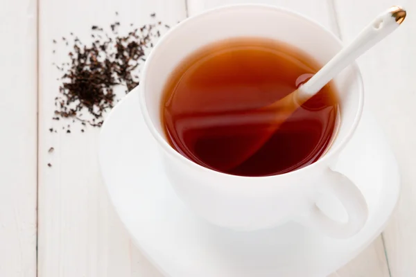 Thé dans une tasse blanche avec une cuillère et des feuilles de thé sur un fond blanc — Photo