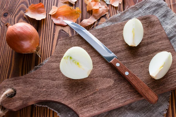 Deska do krojenia z nożem i plasterki cebuli na podłoże drewniane — Zdjęcie stockowe