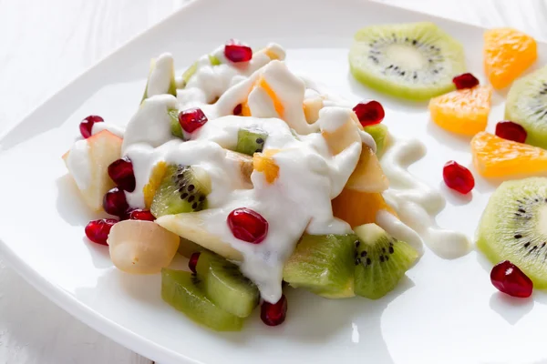 Salade de fruits avec crème glacée sur une assiette blanche décorée de grenade aux baies — Photo