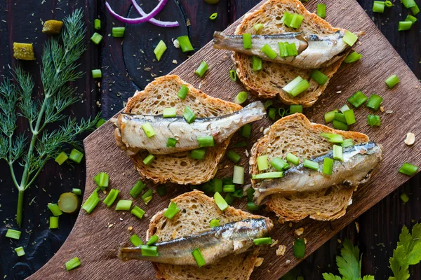 Sandwich with sardines, sprinkle with onions on a cutting board on a black background with fennel and red onion — Stock Photo, Image