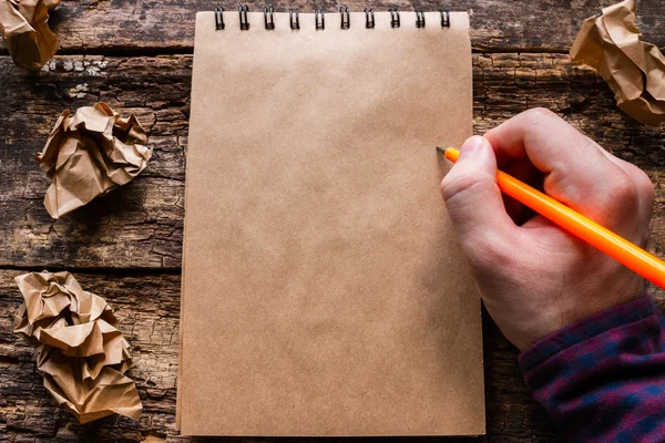 Homem escreve em um caderno sobre um fundo de madeira — Fotografia de Stock