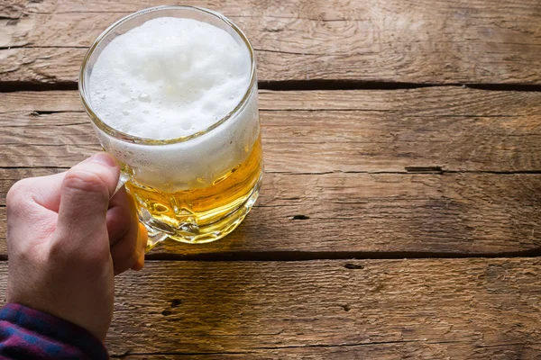 Homem segurando um copo de cerveja em um fundo de madeira — Fotografia de Stock